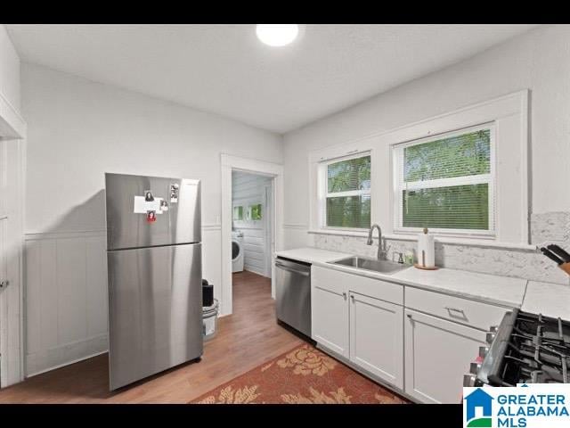 kitchen featuring washer / dryer, white cabinets, appliances with stainless steel finishes, light wood-type flooring, and sink