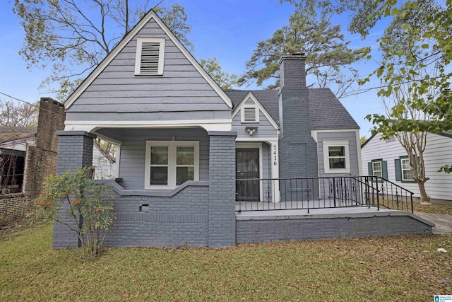 view of front of property with covered porch, a chimney, and a front yard