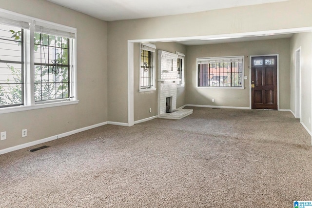 carpeted spare room featuring a brick fireplace and a wealth of natural light