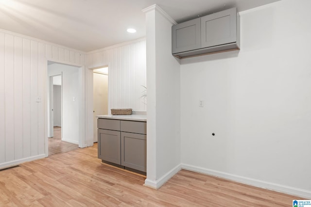 kitchen with ornamental molding, light hardwood / wood-style flooring, gray cabinetry, and wood walls