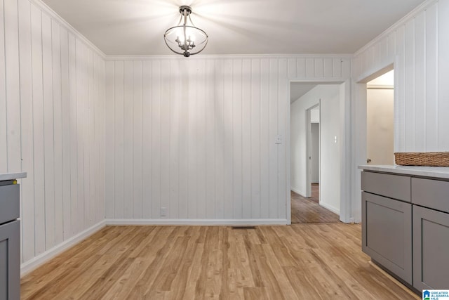 unfurnished dining area featuring an inviting chandelier, ornamental molding, wooden walls, and light hardwood / wood-style floors