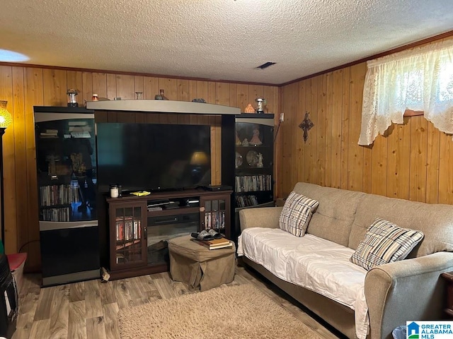 living room featuring light hardwood / wood-style flooring, wood walls, a textured ceiling, and crown molding