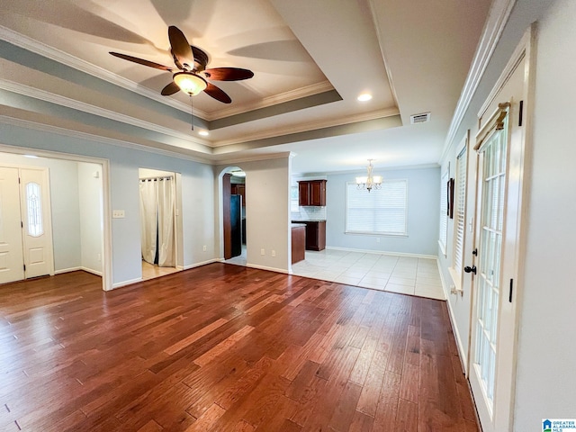 unfurnished living room with ornamental molding, light wood-type flooring, ceiling fan with notable chandelier, and a raised ceiling