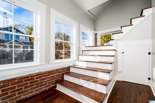 stairs featuring brick wall, vaulted ceiling, and hardwood / wood-style flooring