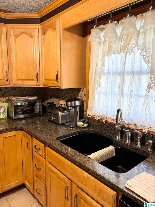 kitchen with backsplash, light tile patterned floors, a textured ceiling, dark stone countertops, and sink