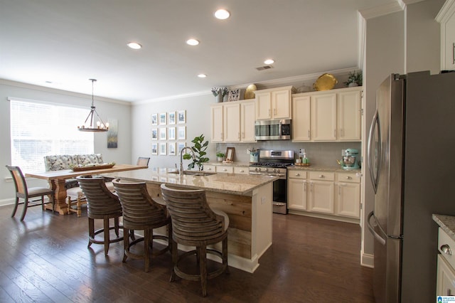 kitchen featuring dark hardwood / wood-style floors, an island with sink, crown molding, pendant lighting, and appliances with stainless steel finishes