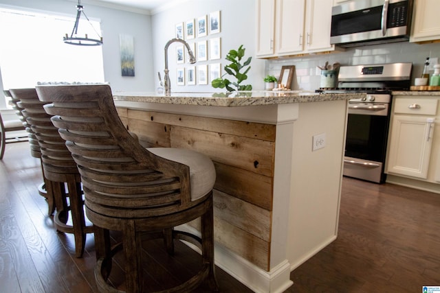 kitchen with white cabinets, light stone counters, stainless steel appliances, dark wood-type flooring, and decorative light fixtures