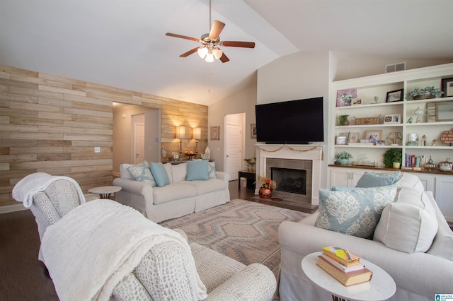 living room featuring ceiling fan, wood walls, dark hardwood / wood-style floors, a tile fireplace, and lofted ceiling with beams