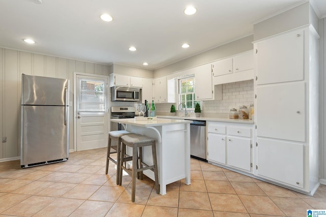 kitchen with a kitchen island, backsplash, white cabinets, light tile patterned flooring, and appliances with stainless steel finishes