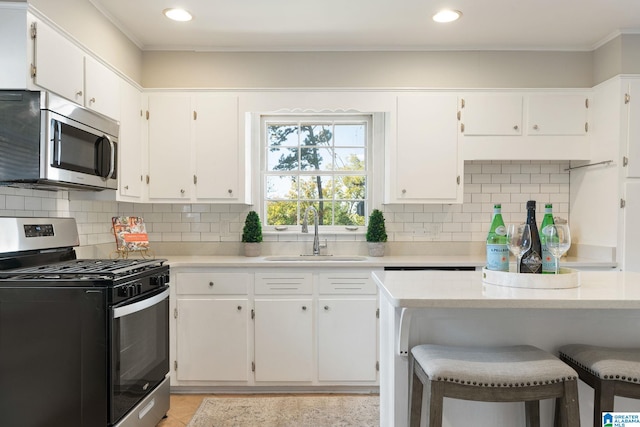 kitchen with appliances with stainless steel finishes, sink, white cabinets, decorative backsplash, and a breakfast bar area