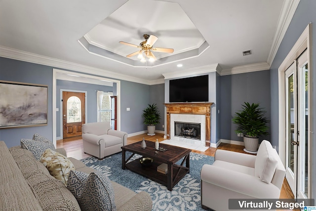 living room with a raised ceiling, ornamental molding, light wood-type flooring, and ceiling fan