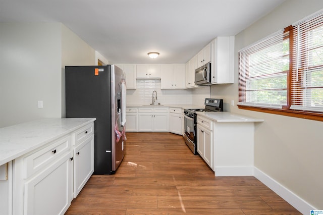 kitchen with white cabinets, backsplash, light wood-type flooring, stainless steel appliances, and light stone counters