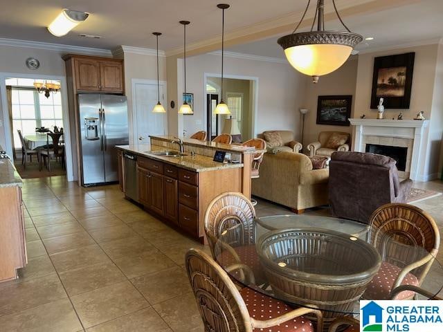 kitchen with light stone countertops, sink, appliances with stainless steel finishes, decorative light fixtures, and ornamental molding