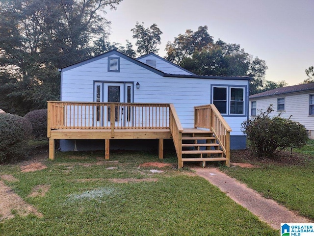 back house at dusk featuring a lawn and a deck