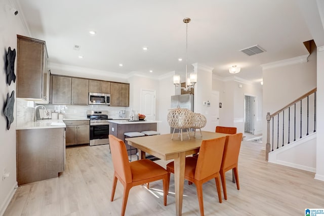 dining space with light hardwood / wood-style floors, crown molding, a chandelier, and sink