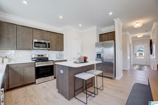 kitchen featuring backsplash, a kitchen island, light hardwood / wood-style floors, crown molding, and stainless steel appliances