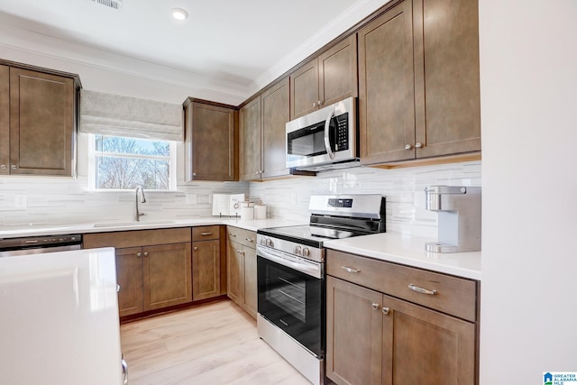 kitchen featuring backsplash, ornamental molding, sink, appliances with stainless steel finishes, and light hardwood / wood-style floors