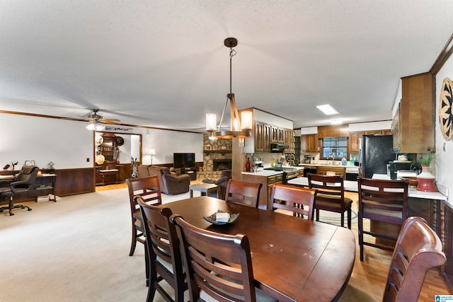 carpeted dining area featuring a stone fireplace, ornamental molding, a textured ceiling, and ceiling fan