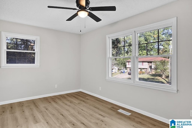 empty room with ceiling fan, a textured ceiling, light hardwood / wood-style flooring, and plenty of natural light