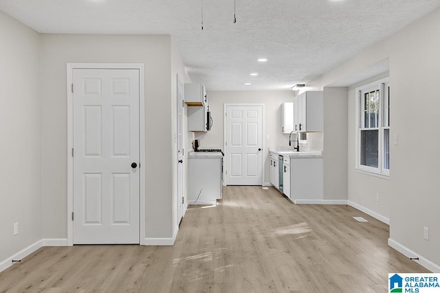 kitchen featuring white cabinets, a textured ceiling, stainless steel dishwasher, light hardwood / wood-style floors, and sink