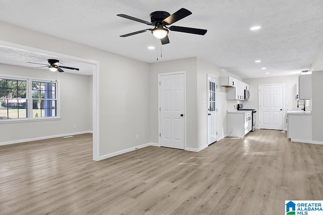 unfurnished living room with light hardwood / wood-style flooring, a textured ceiling, sink, and ceiling fan