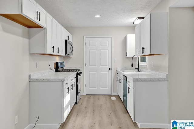 kitchen with appliances with stainless steel finishes, white cabinetry, a textured ceiling, light hardwood / wood-style flooring, and sink