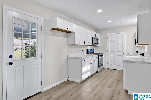 kitchen featuring a textured ceiling, white cabinetry, stainless steel appliances, light hardwood / wood-style floors, and sink