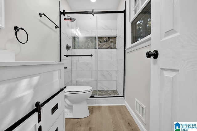 bathroom featuring toilet, hardwood / wood-style flooring, a shower with shower door, and vanity