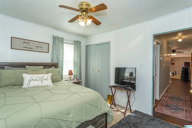 bedroom featuring wood walls, ceiling fan, a textured ceiling, a closet, and dark hardwood / wood-style flooring