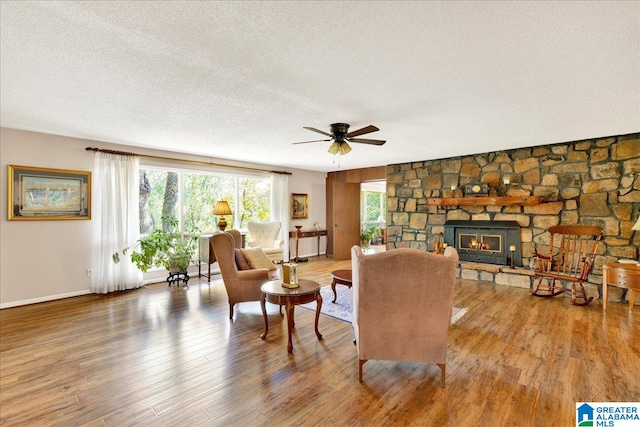 living room featuring ceiling fan, a stone fireplace, wood-type flooring, and a textured ceiling