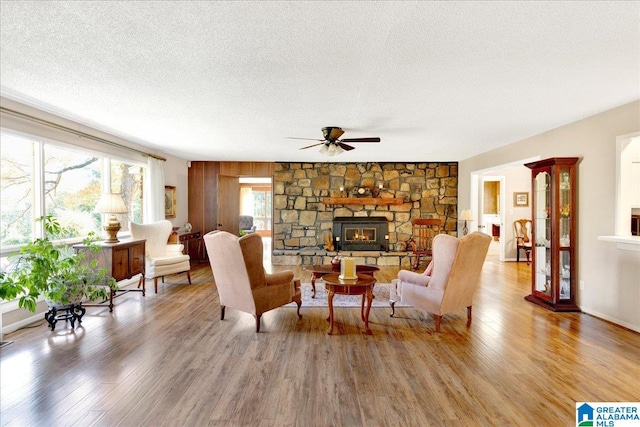 living room featuring a stone fireplace, a textured ceiling, hardwood / wood-style flooring, and ceiling fan