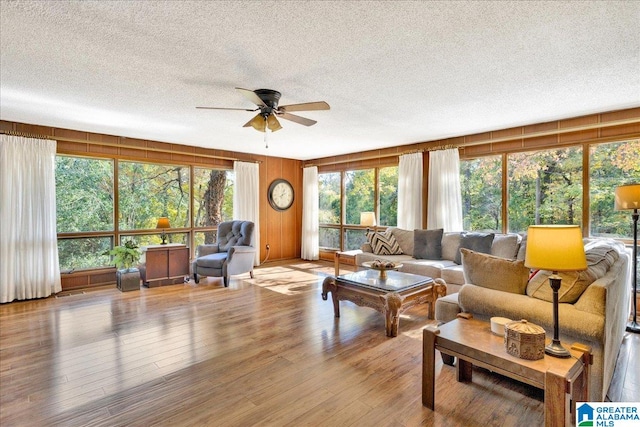 living room featuring light hardwood / wood-style floors, a textured ceiling, wooden walls, and ceiling fan