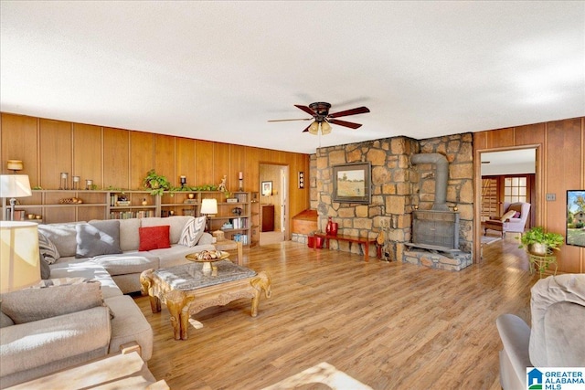 living room with ceiling fan, a textured ceiling, a wood stove, and light hardwood / wood-style flooring