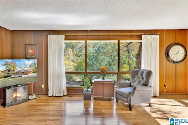 sitting room featuring wooden walls, light hardwood / wood-style flooring, and a textured ceiling