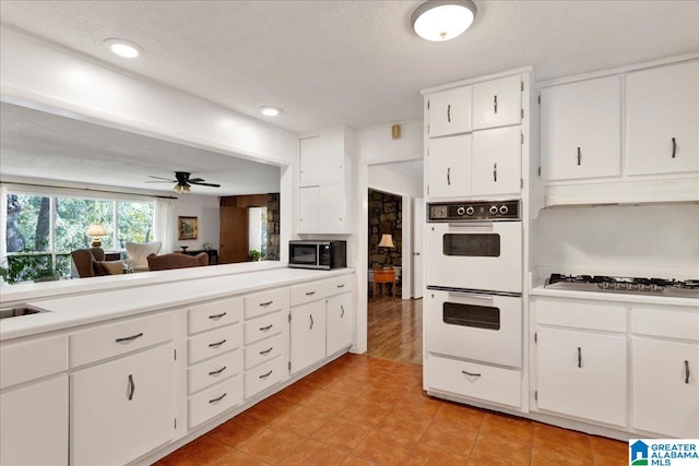 kitchen featuring stainless steel gas cooktop, white cabinetry, double oven, and ceiling fan