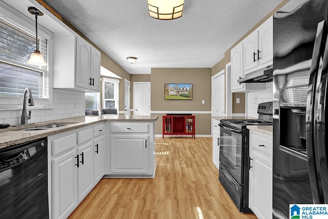 kitchen featuring black appliances, sink, light wood-type flooring, decorative light fixtures, and white cabinets