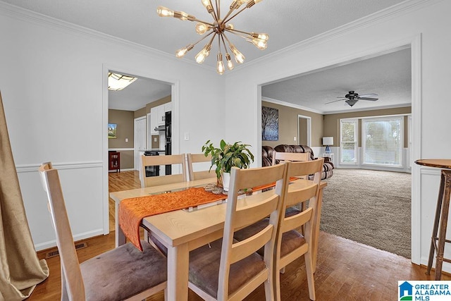 carpeted dining room with crown molding and ceiling fan with notable chandelier