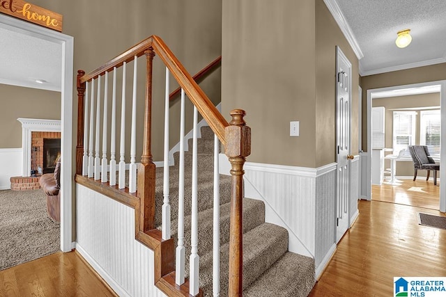 stairs featuring wood-type flooring, a textured ceiling, a fireplace, and ornamental molding