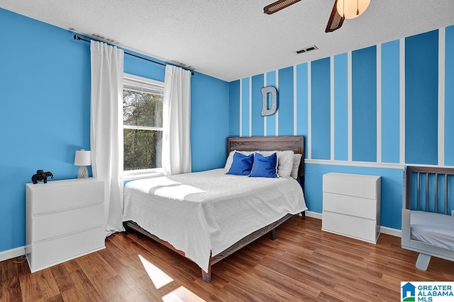 bedroom with a textured ceiling, wood-type flooring, and ceiling fan