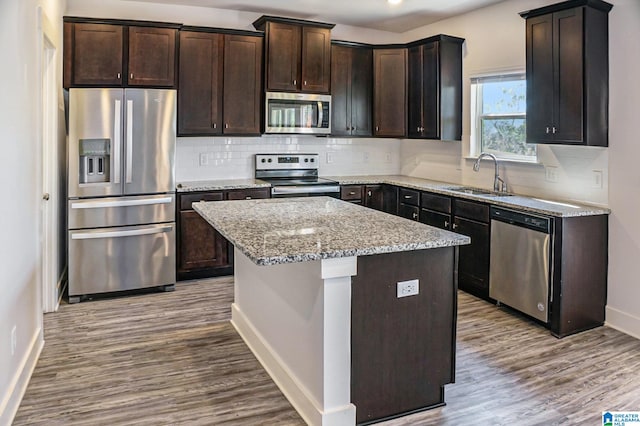 kitchen with a kitchen island, wood-type flooring, stainless steel appliances, sink, and light stone counters