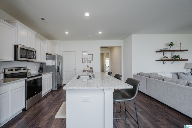 kitchen with appliances with stainless steel finishes, a kitchen island with sink, a kitchen breakfast bar, and dark hardwood / wood-style flooring