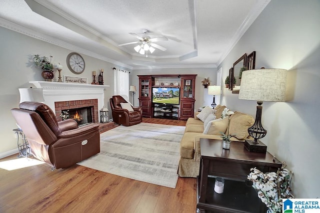 living room with a fireplace, hardwood / wood-style flooring, ceiling fan, a tray ceiling, and crown molding