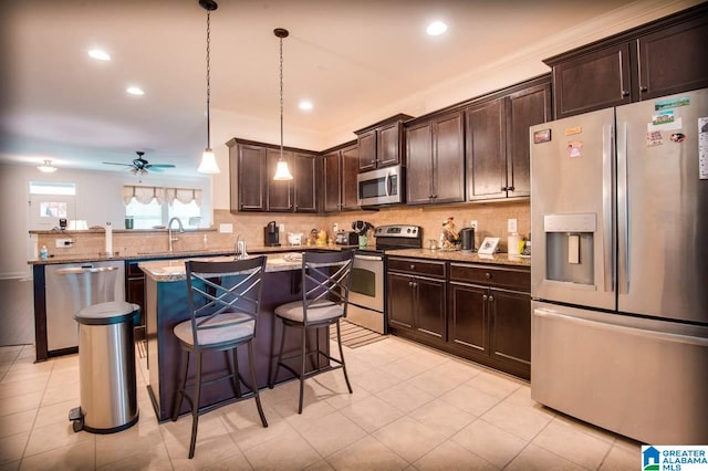 kitchen featuring appliances with stainless steel finishes, kitchen peninsula, decorative light fixtures, light stone counters, and a breakfast bar