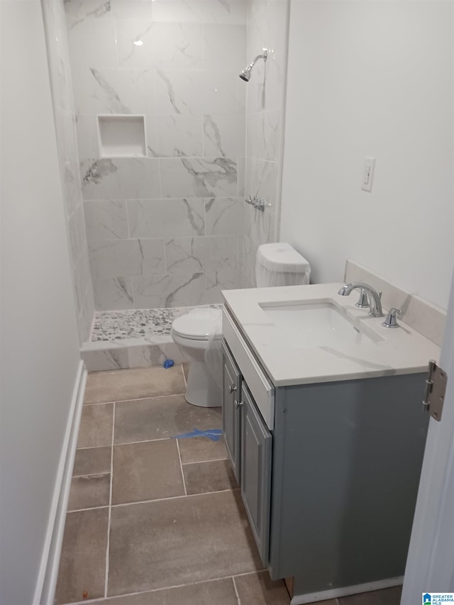 bathroom featuring vanity, toilet, tiled shower, and tile patterned flooring