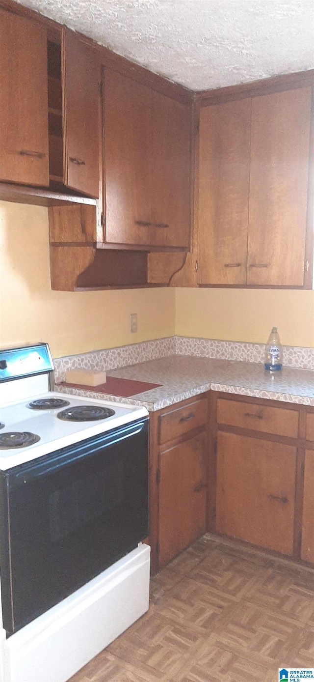 kitchen featuring white range with electric cooktop, brown cabinets, a textured ceiling, and light countertops
