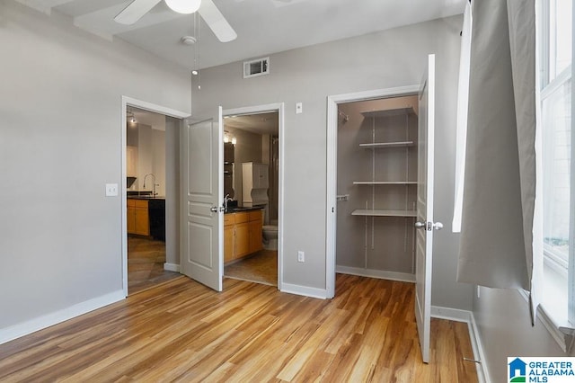 unfurnished bedroom with sink, light wood-type flooring, a walk in closet, a closet, and ceiling fan