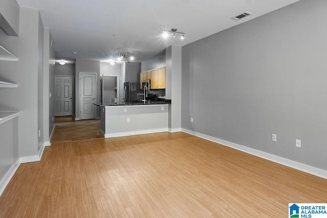 kitchen featuring light brown cabinetry, sink, kitchen peninsula, black fridge, and light hardwood / wood-style floors