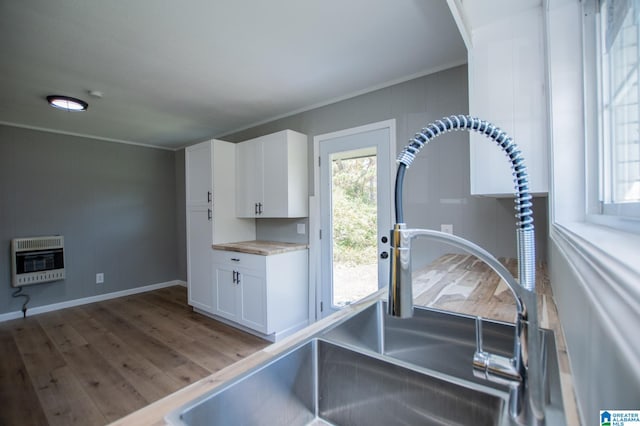 kitchen featuring hardwood / wood-style floors, white cabinetry, heating unit, and crown molding