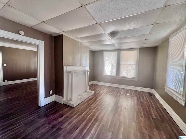 unfurnished living room featuring a paneled ceiling, wood walls, dark hardwood / wood-style flooring, and a brick fireplace