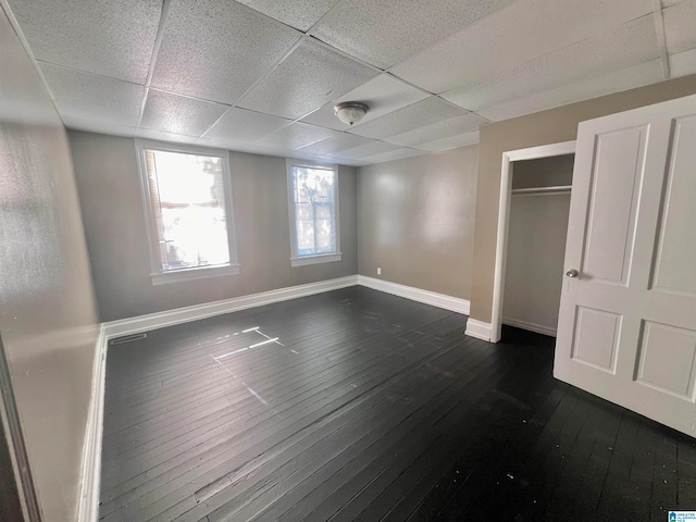 unfurnished bedroom with a closet, a paneled ceiling, and dark wood-type flooring